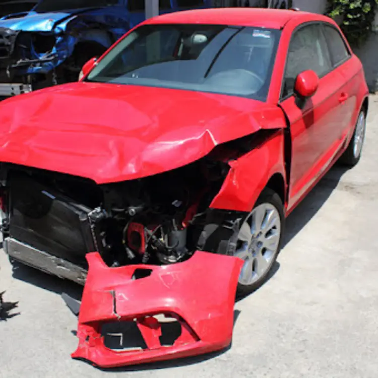 Auto Siniestrado: Primer plano de un Audi rojo con daño frontal severo, el parachoques desprendido y el radiador expuesto, mostrando que es un auto siniestrado.