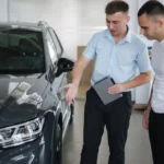 Compro tu coche con Autoefectivo: Asesor mostrando y explicando detalles de la tasación de un vehículo oscuro a un cliente en el concesionario.