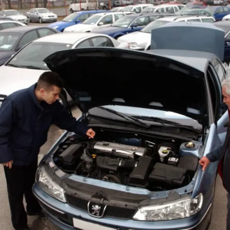 Cotiza tu auto: Tasador profesional revisando el motor de un Peugeot azul con el capó abierto en un lote de vehículos para ofrecer una cotización justa.